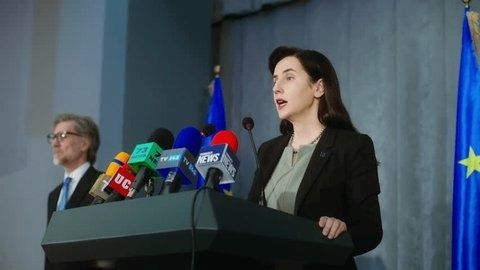 Kvinne taler ved podiet foran en samling presse­mikrofoner
